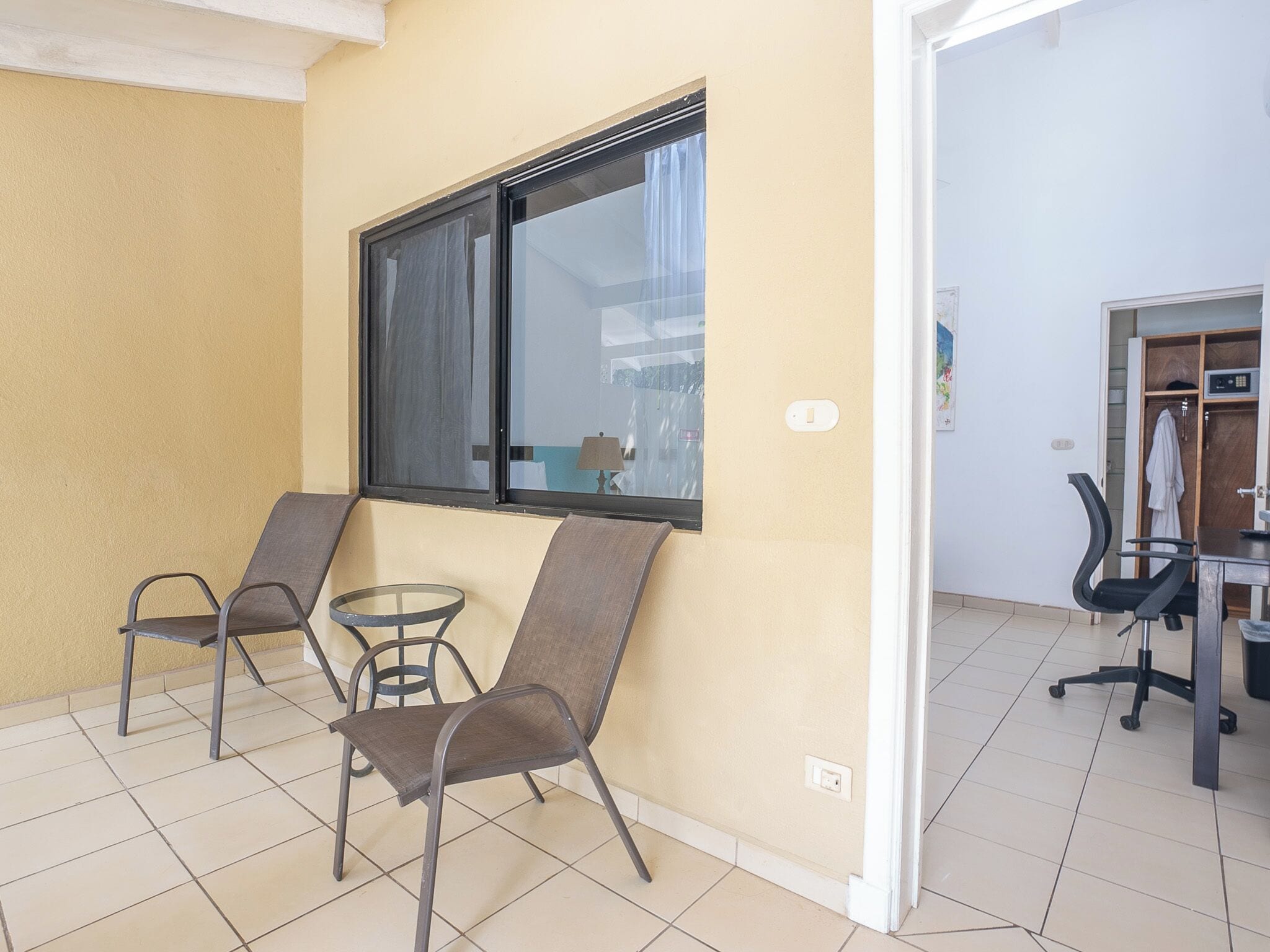 Una habitación con dos sillas, una mesita y un ventanal con cortinas.