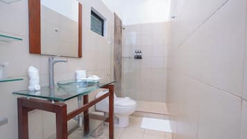 A modern bathroom with a glass sink, wooden vanity, a toilet, and a shower area.