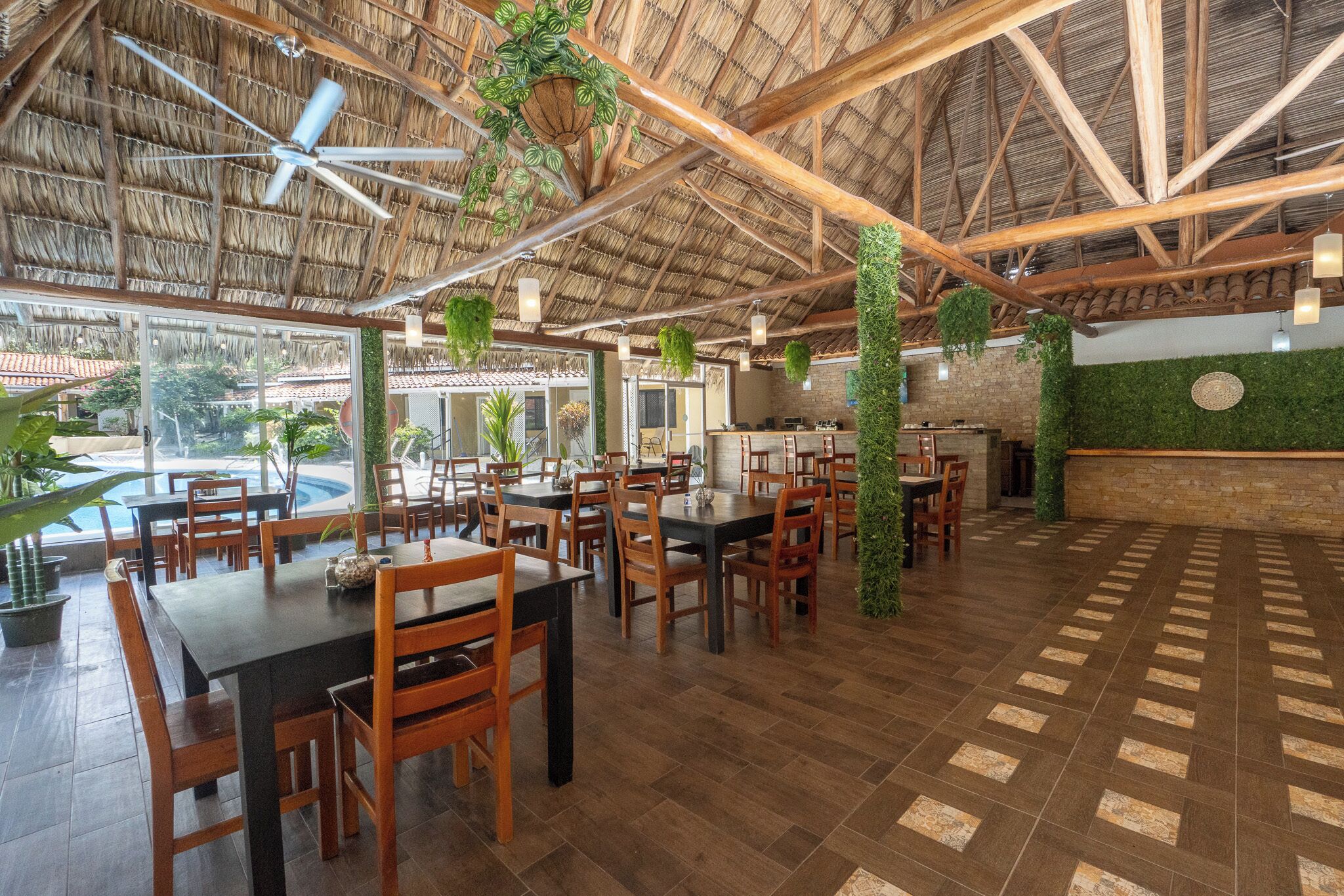 Un comedor amplio con mesas y sillas de madera, techo de paja y plantas colgantes.