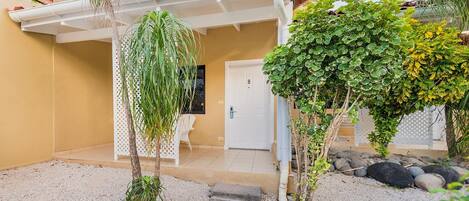 A covered patio area with a white door, a white chair, and a small garden with rocks and plants.