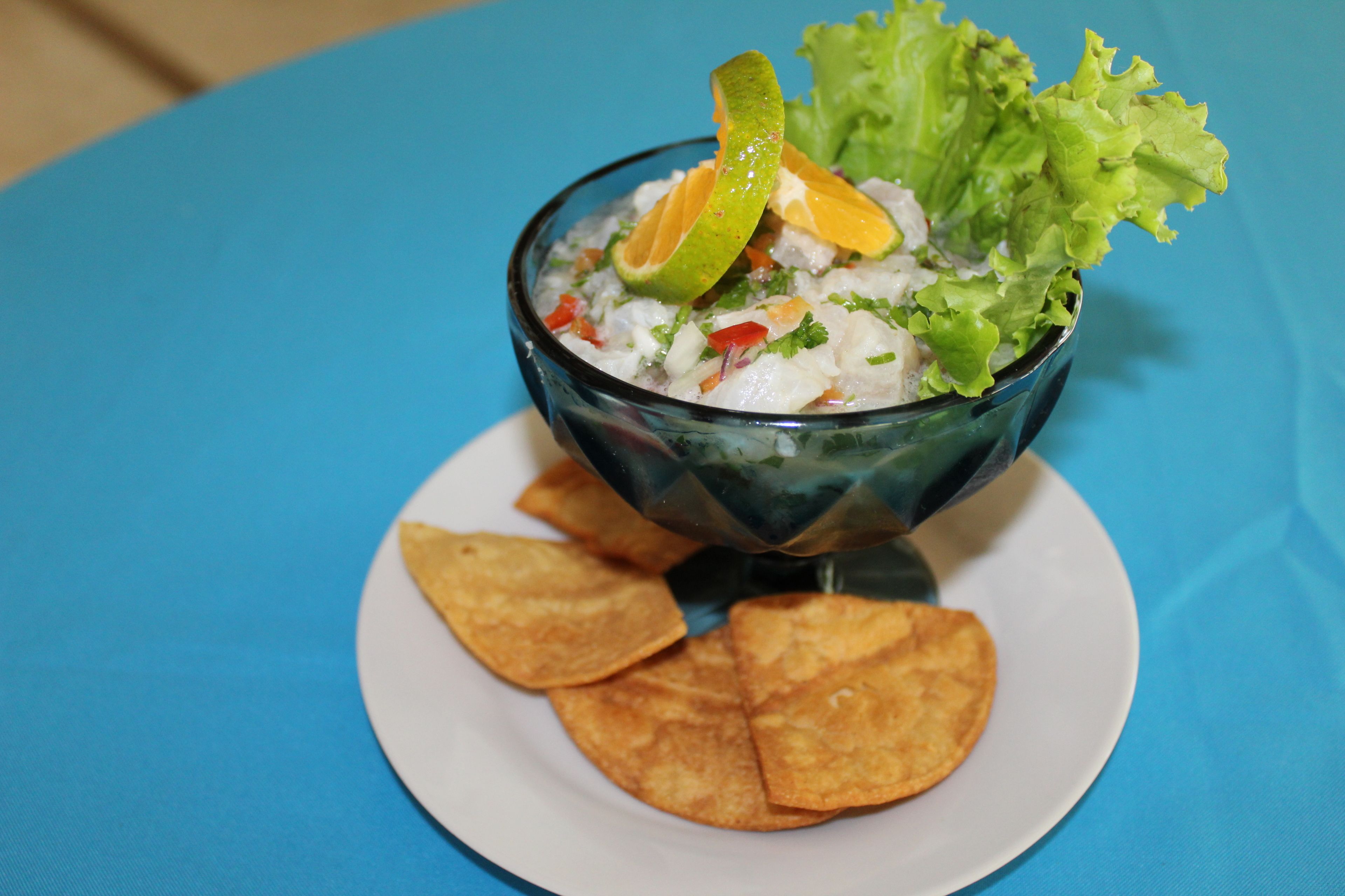 A bowl of seafood salad with lime and lettuce on a white plate, accompanied by tortilla chips.
