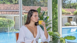 A person sitting by a pool with a glass of orange juice, a plate of food, and a plant on the table. - Seis Playas Hotel (Tamarindo)