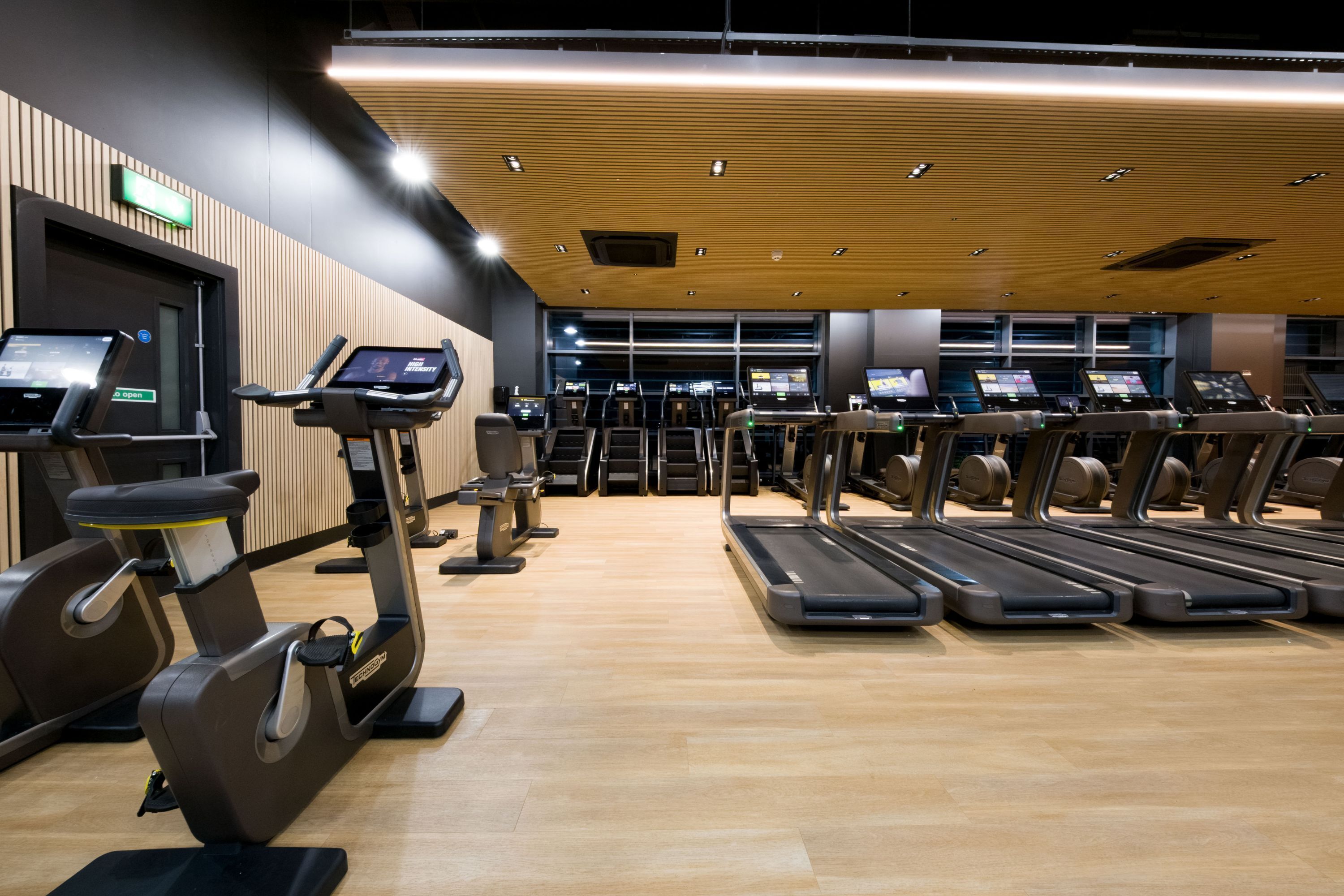 A gym with exercise equipment, including treadmills and stationary bikes, and a wooden floor.