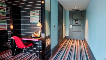 Habitación de hotel con alfombra a rayas, una silla roja, un escritorio con lámpara y un rincón americano.
