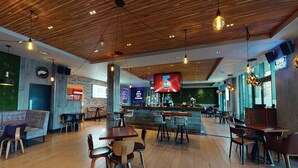 Un restaurante amplio con piso de madera, zona de bar y una pantalla grande que muestra un menú.
