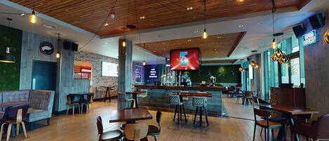 A spacious restaurant with wooden flooring, a bar area, and a large screen displaying a menu.