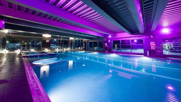 Una piscina interior con diseño moderno, que cuenta con un amplio espacio para nadar y una sección cubierta con techo inclinado.