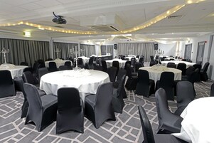 Un salón de banquetes con mesas redondas, sillas negras y manteles blancos.