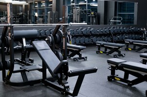 Un gimnasio con equipamiento de levantamiento de pesas, mancuernas y bancos.
