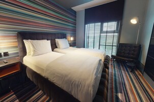 Una habitación de hotel con una cama grande, una silla y un muro a rayas.