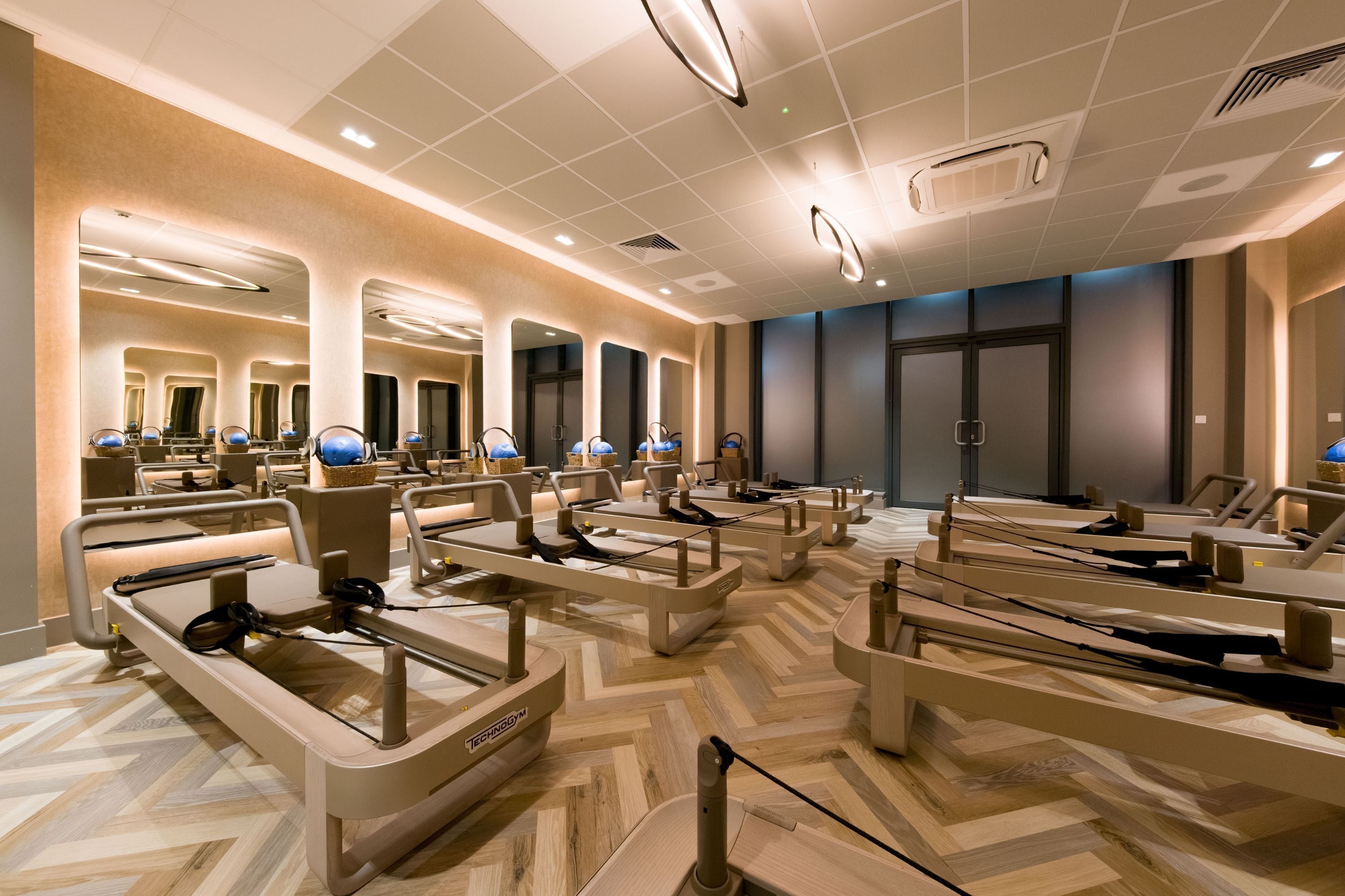 A modern hotel lobby with multiple massage chairs, a herringbone-patterned floor, and a large mirror wall.