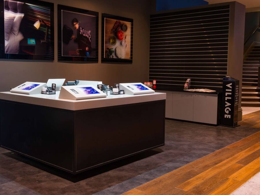 A modern reception desk with digital displays, framed artwork on the wall, and a staircase in the background.