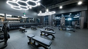 Un gimnasio con equipo de ejercicio, bancos y un espejo grande.