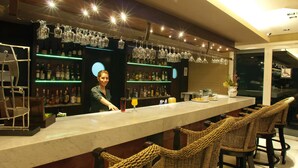 Eine Bar mit einer langen Theke, Korbstühlen und Regalen voller Flaschen und Gläsern.