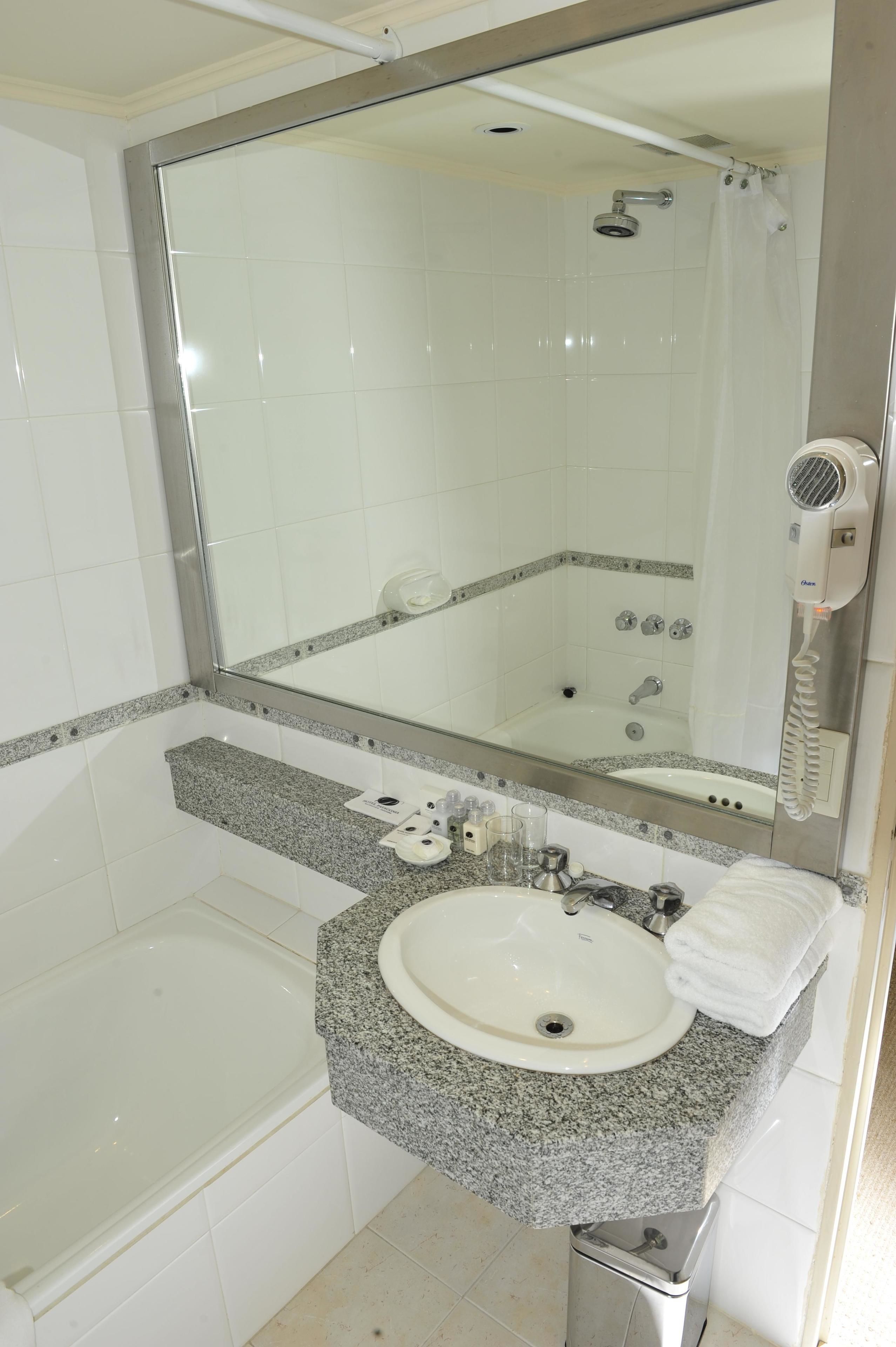 Une salle de bain avec un lavabo blanc, un comptoir en granit, un miroir et un espace douche.