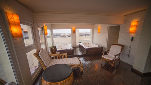 Ein geräumiger Balkon mit zwei Whirlpools, Korbmöbeln und Blick auf die Stadt.