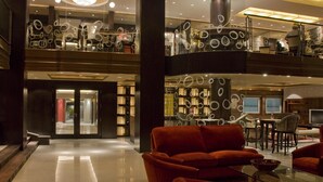 Eine geräumige, moderne Hotelhalle mit einer roten Couch, einem Glastisch und einem Essbereich mit Korbstühlen.