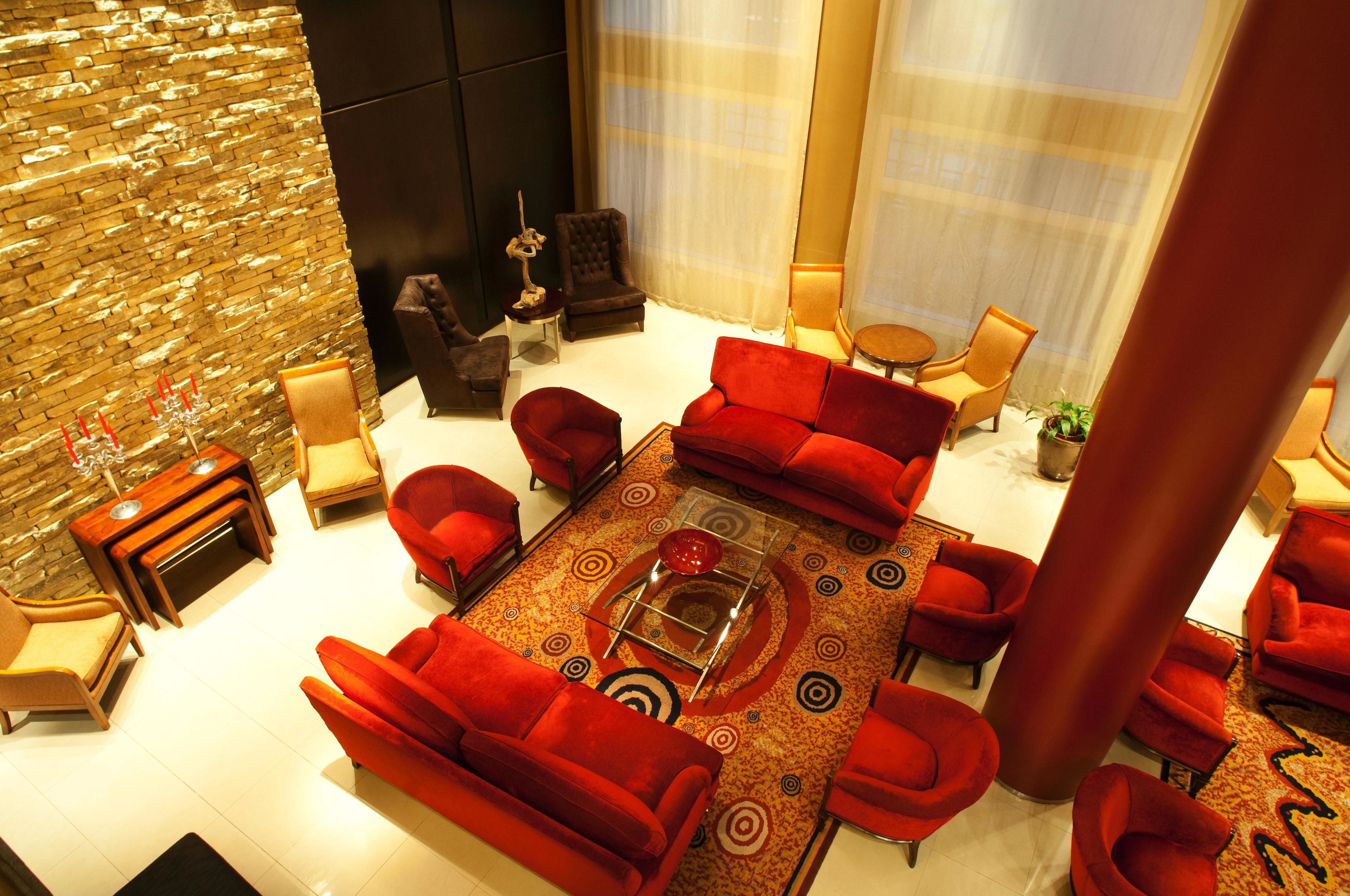 Un salon moderne avec des canapés rouges, une table basse en verre et un mur d’accent en pierre.