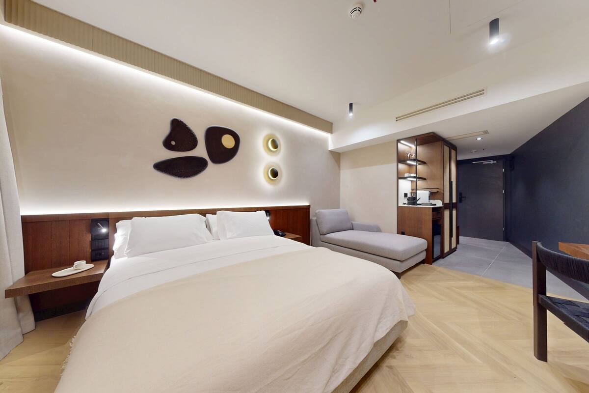 A modern hotel room with a large bed, a desk, and a seating area.