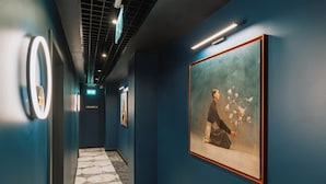 A hallway with a patterned floor, framed artwork on the walls, and an elevator sign. - Hotel Maison Orient (Bucharest)