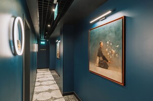 A hallway with a patterned floor, framed artwork on the walls, and an elevator sign.