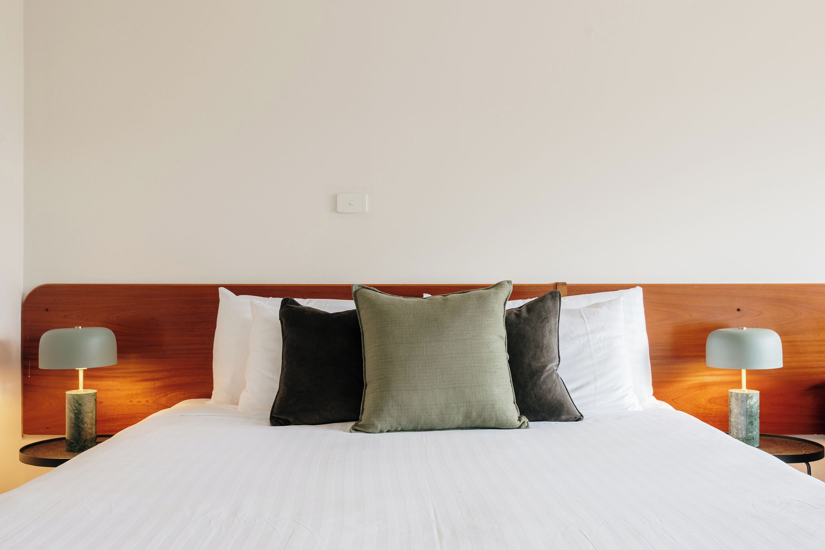 A neatly made bed with white linens, a wooden headboard, and three pillows in different colors.