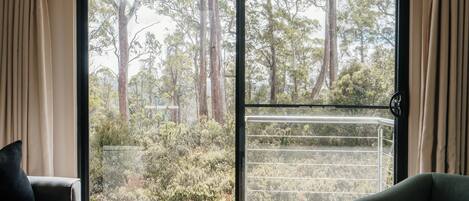 A room with a large sliding glass door leading to a balcony with a view of tall trees and shrubs.