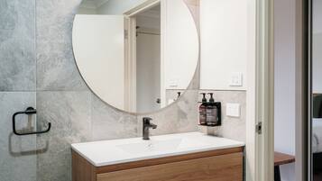 Une salle de bain avec un miroir rond, un lavabo blanc, des meubles en bois et un porte-serviettes.