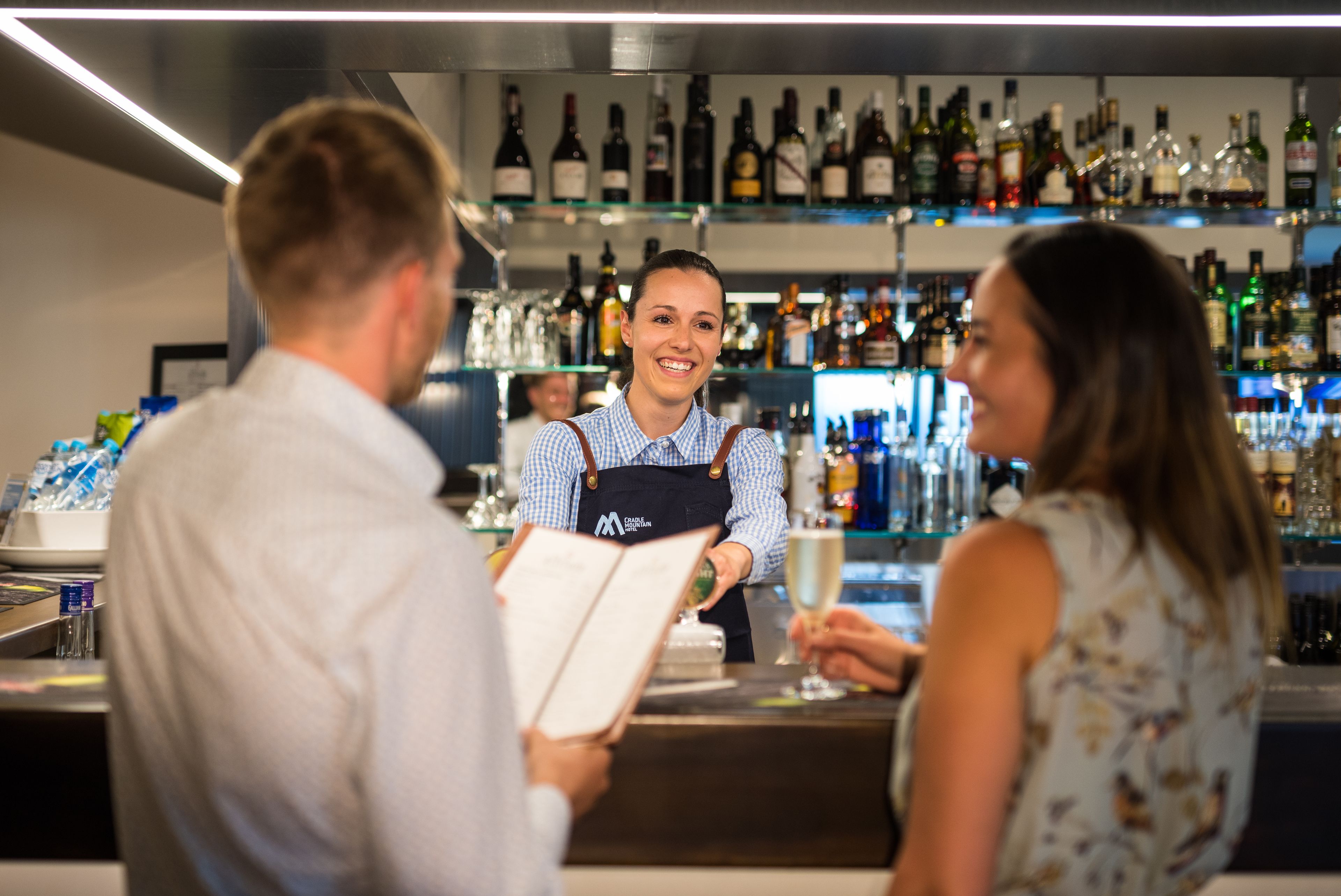 A bar area with a bartender, shelves of bottles, and a menu.