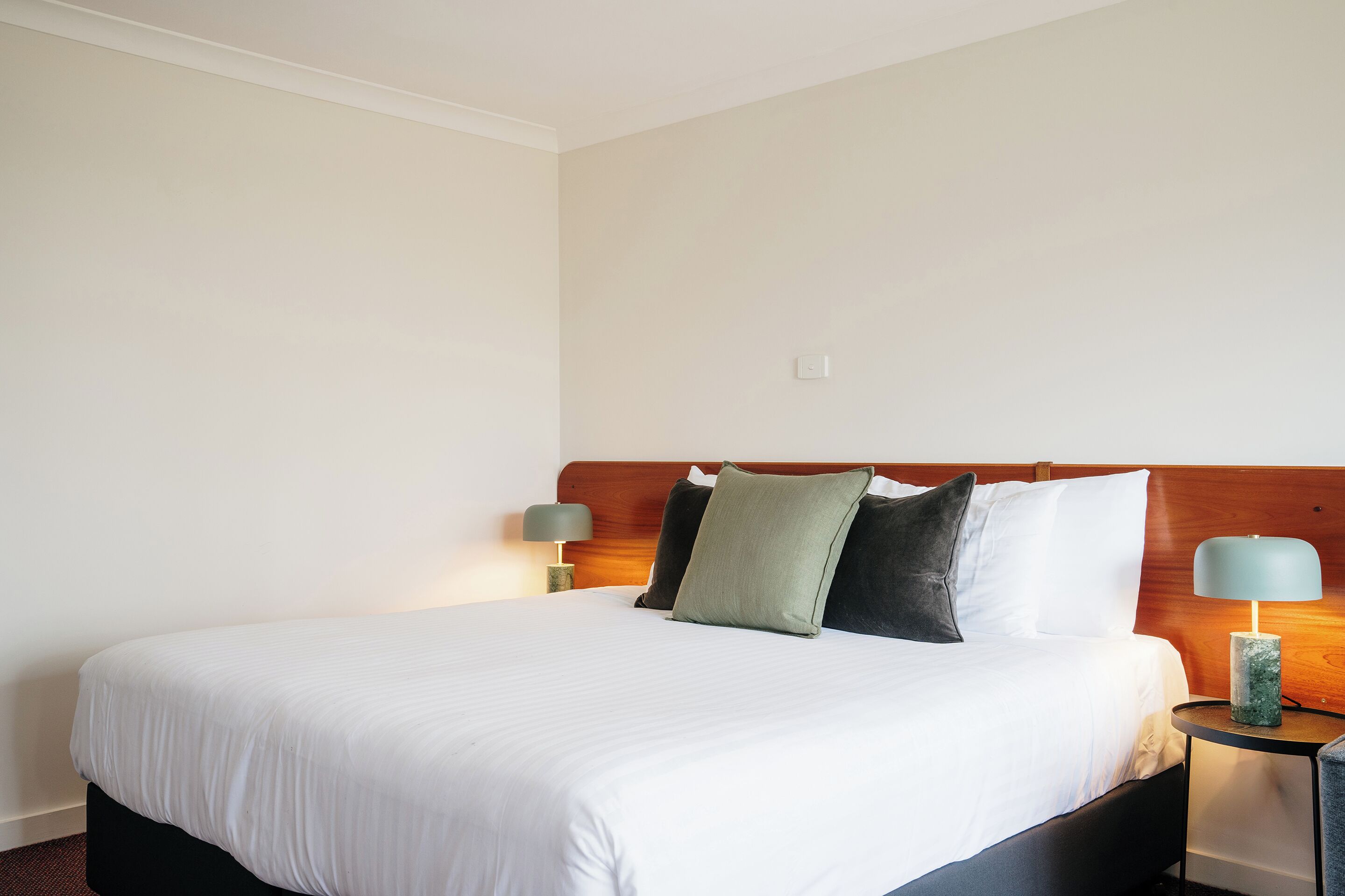 A neatly made bed with white bedding, a wooden headboard, and two bedside lamps.