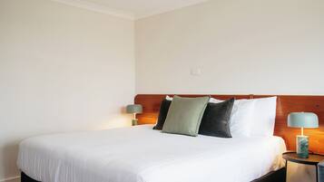 Una cama bien hecha con ropa blanca, cabecera de madera y dos lámparas de noche.