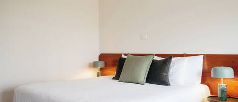 A neatly made bed with white bedding, a wooden headboard, and two bedside lamps.