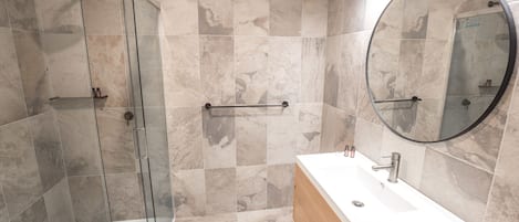 Un baño moderno con cabina de ducha de vidrio, tocador de madera y un espejo grande.