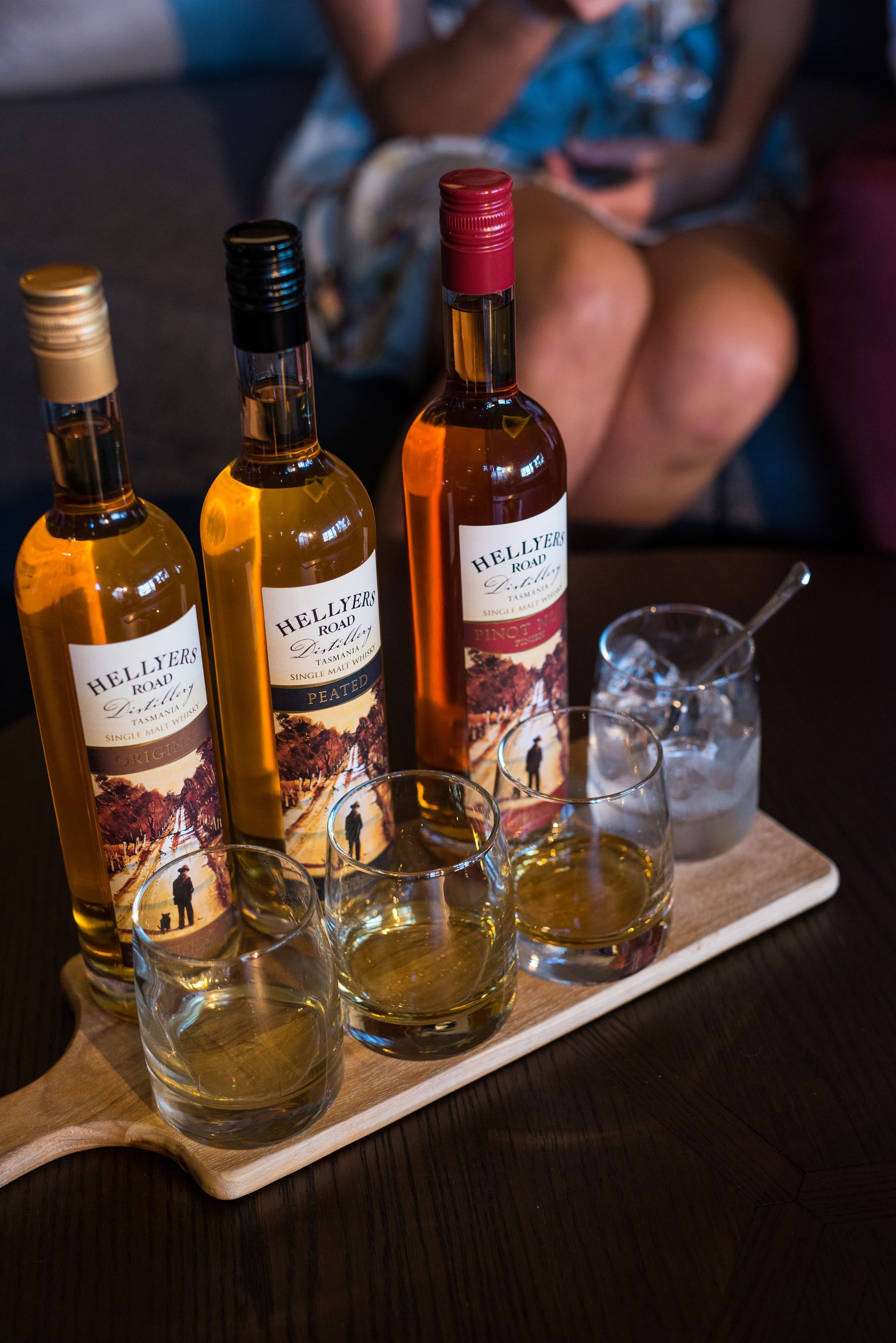 Tres botellas de vino single malt Helliers Road y cuatro copas sobre una bandeja de madera.