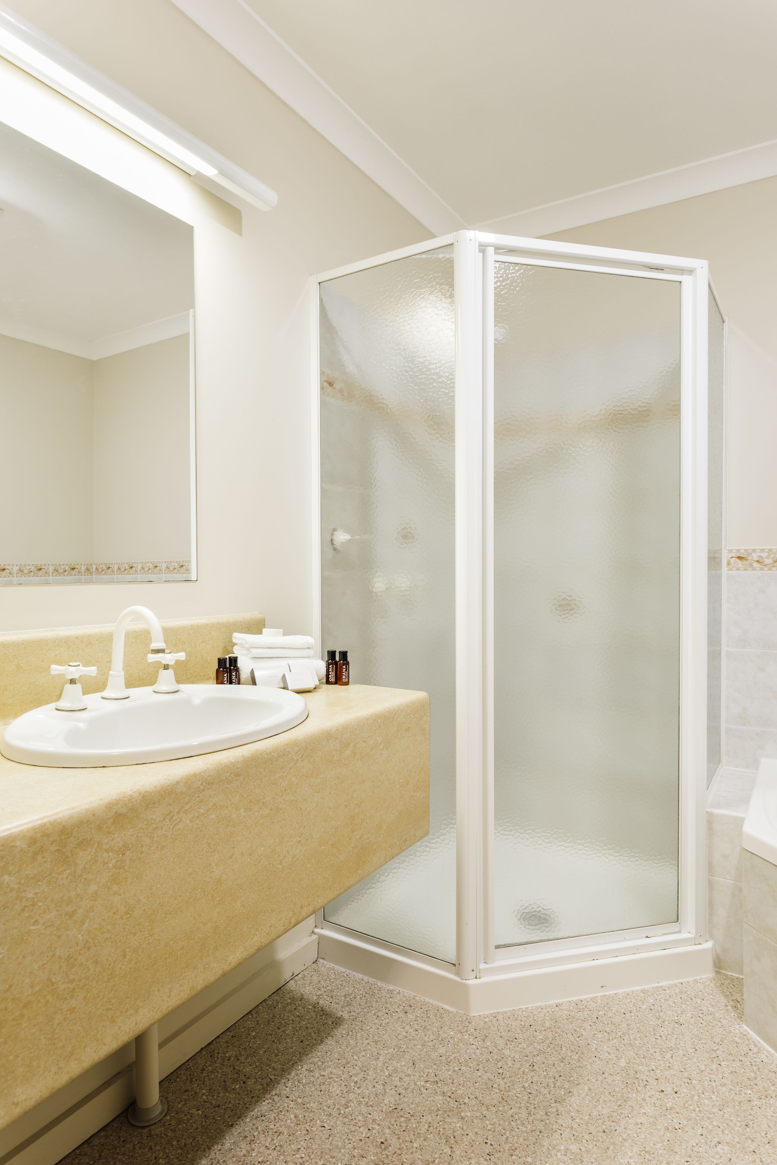 Une salle de bain avec un lavabo blanc, un miroir et une douche fermée par des parois de verre.