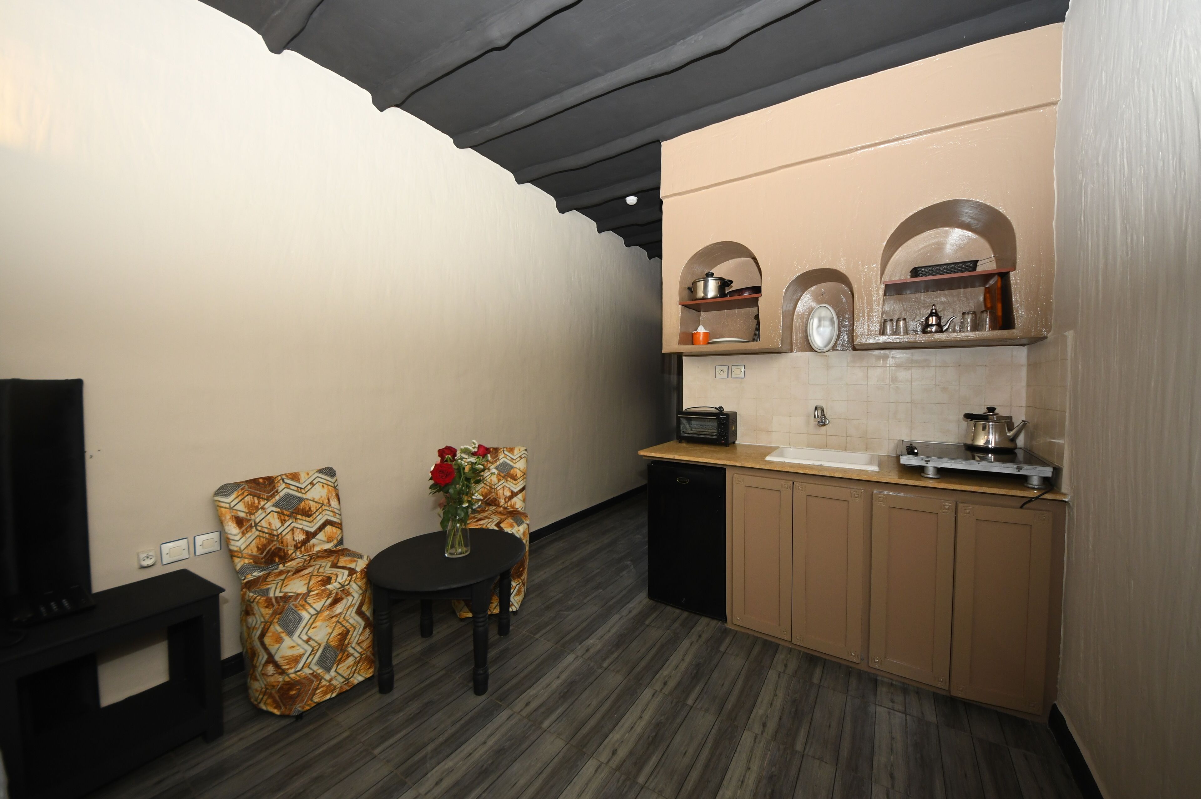 A compact kitchen with a dining area, a television, and a patterned chair.