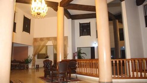 Un amplio vestíbulo con techos altos, un candelabro, columnas de madera y un mostrador de recepción.