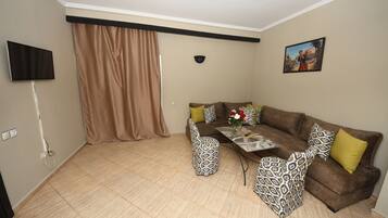 Una sala de estar con un sofá marrón, sillones estampados, una mesa de centro y un televisor montado en la pared.