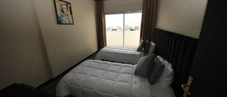 Habitación de hotel con cama, ventana con cortinas, lámpara de pared y puerta con pomo dorado.