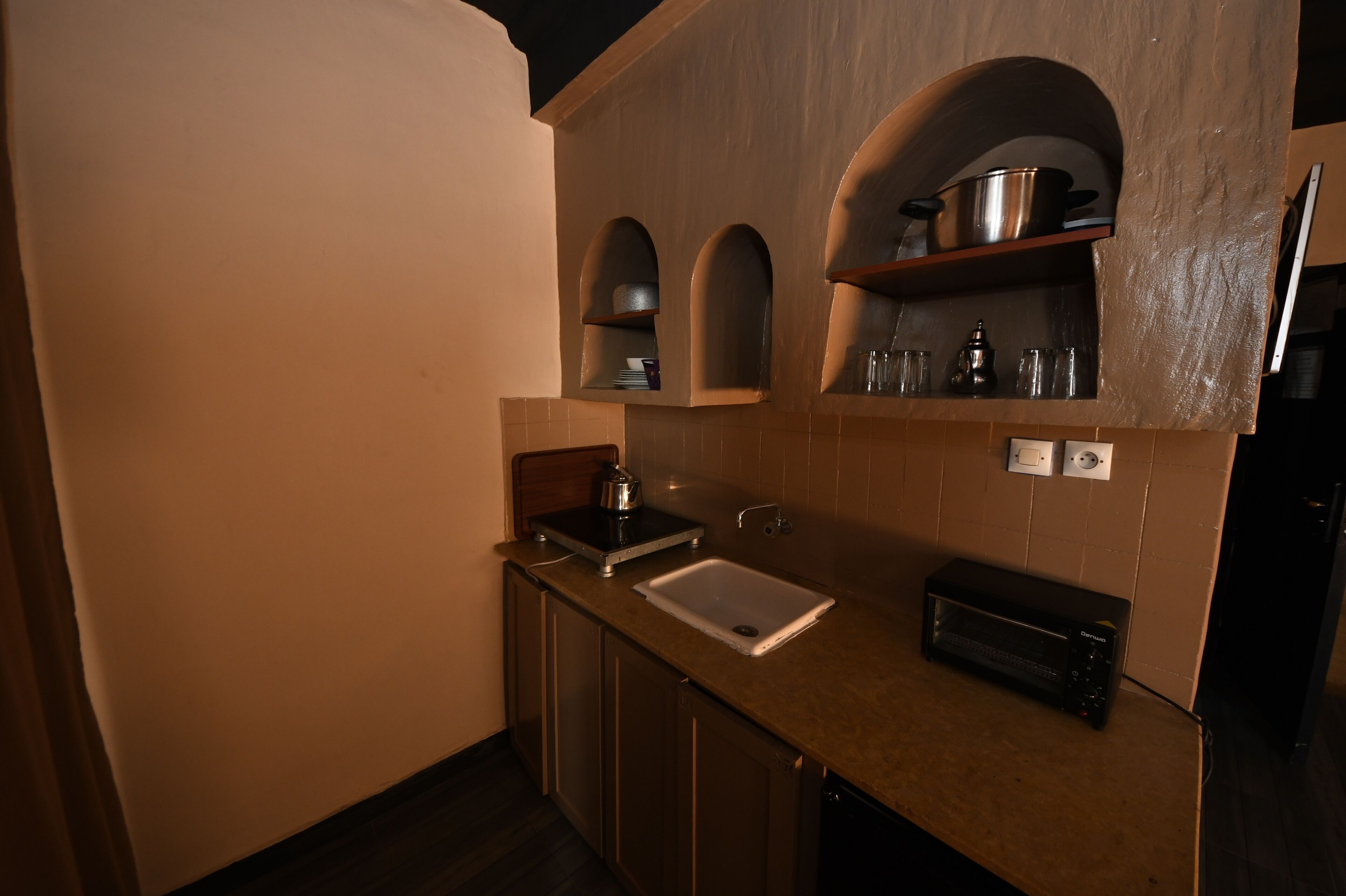 A kitchen with a sink, a toaster, and a microwave. There are two shelves above the sink with kitchenware.