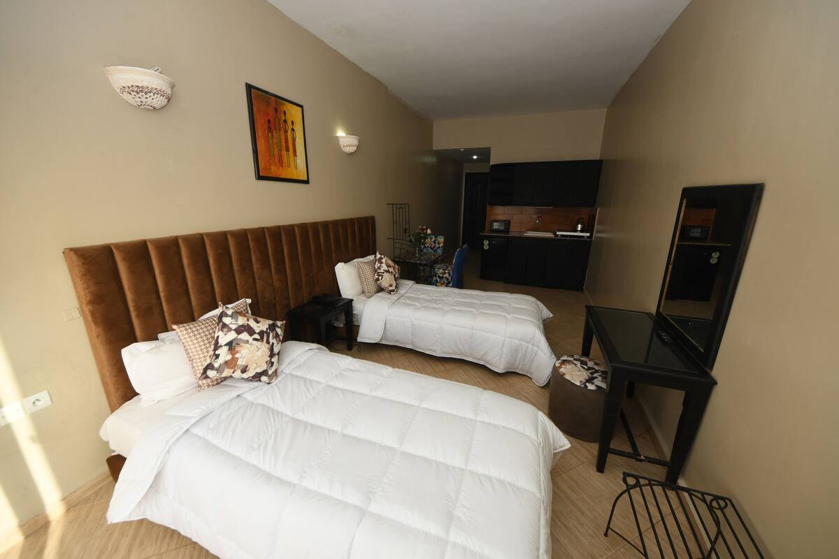 A hotel room with two beds, a desk, a chair, a small table, and a kitchenette.