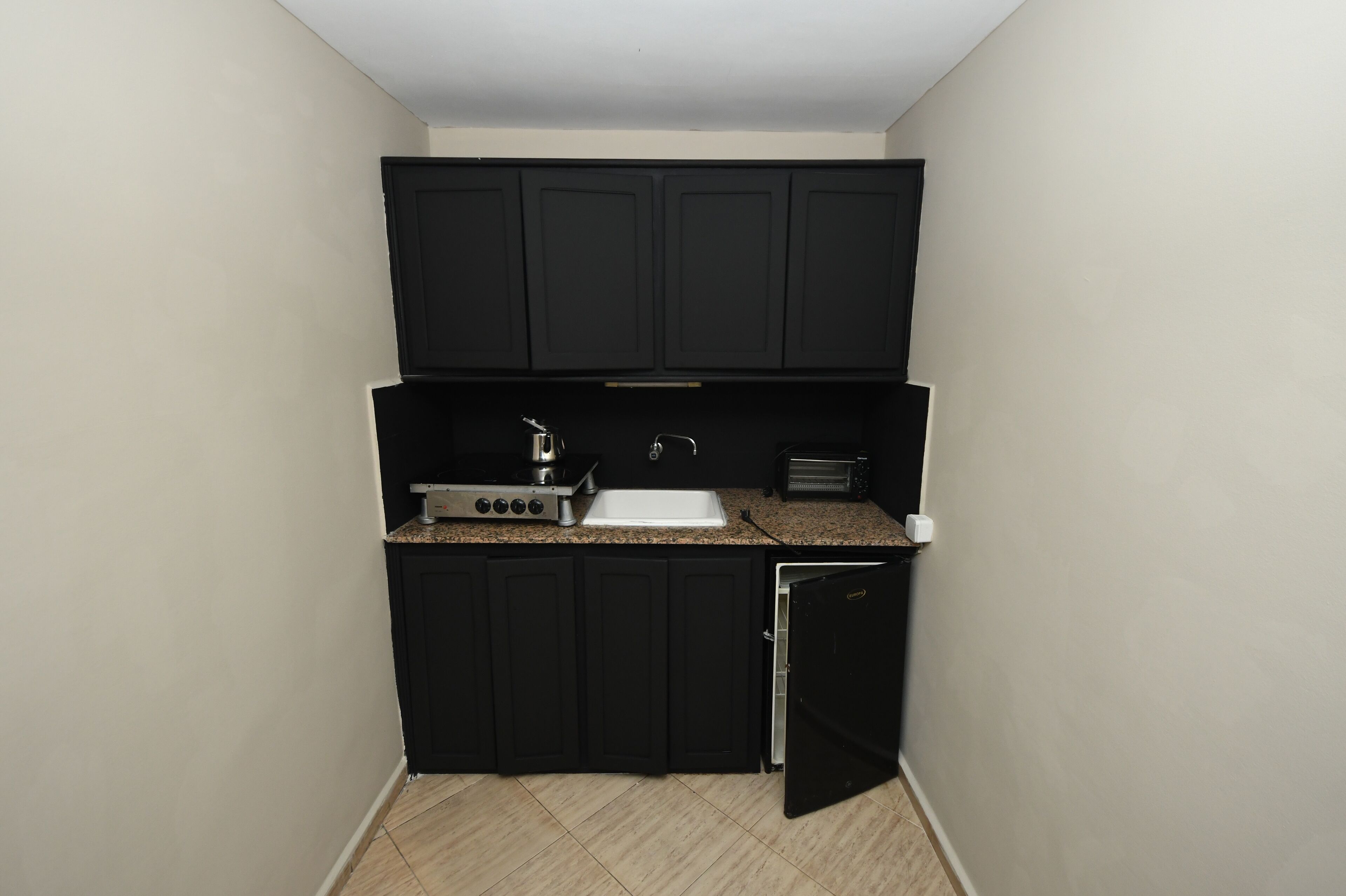 A compact kitchen with black cabinets, a built-in stove, a sink, and a toaster.