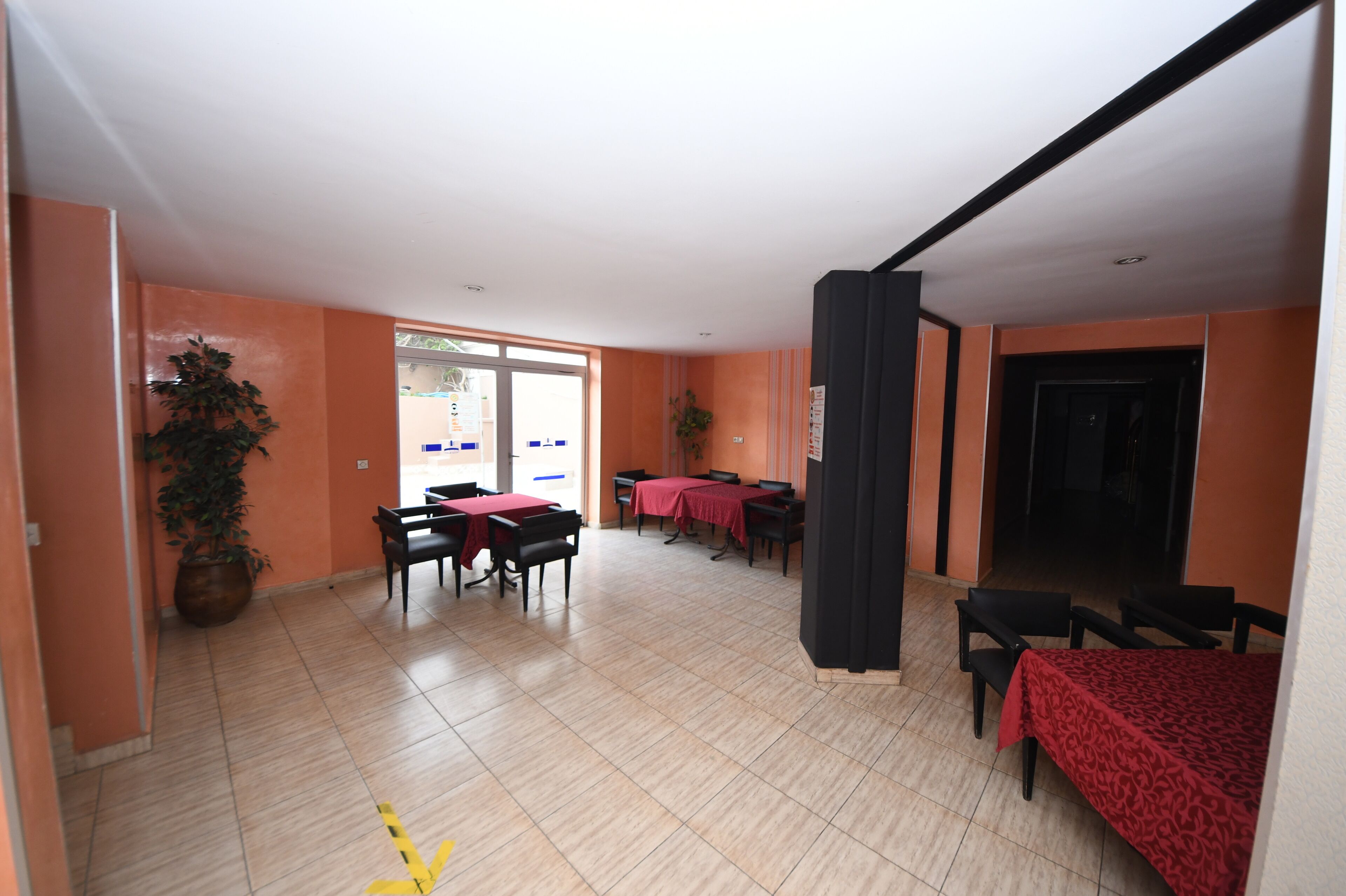 A spacious indoor area with multiple tables and chairs, a potted plant, and a door leading outside.