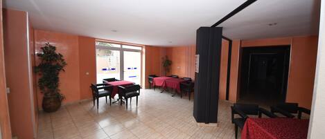 A spacious indoor area with multiple tables and chairs, a potted plant, and a door leading outside.