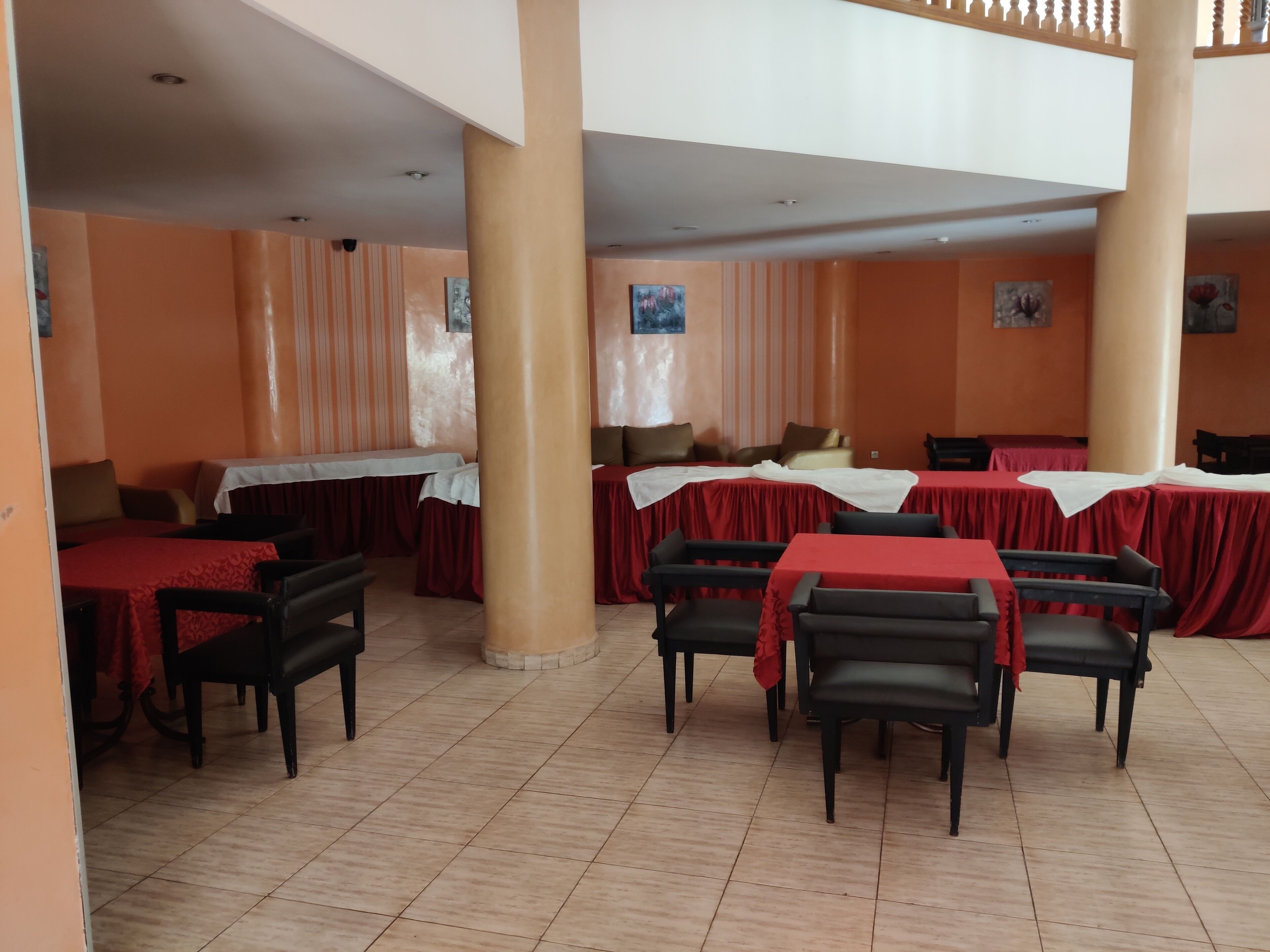 A dining area with tables covered in red tablecloths, black chairs, and orange walls.