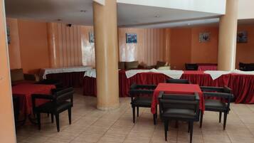 A dining area with tables covered in red tablecloths, black chairs, and orange walls.
