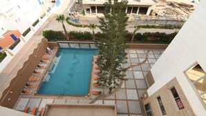Vista aérea de un hotel con piscina rodeada de sillas de descanso, una palmera y vistas de los edificios circundantes.