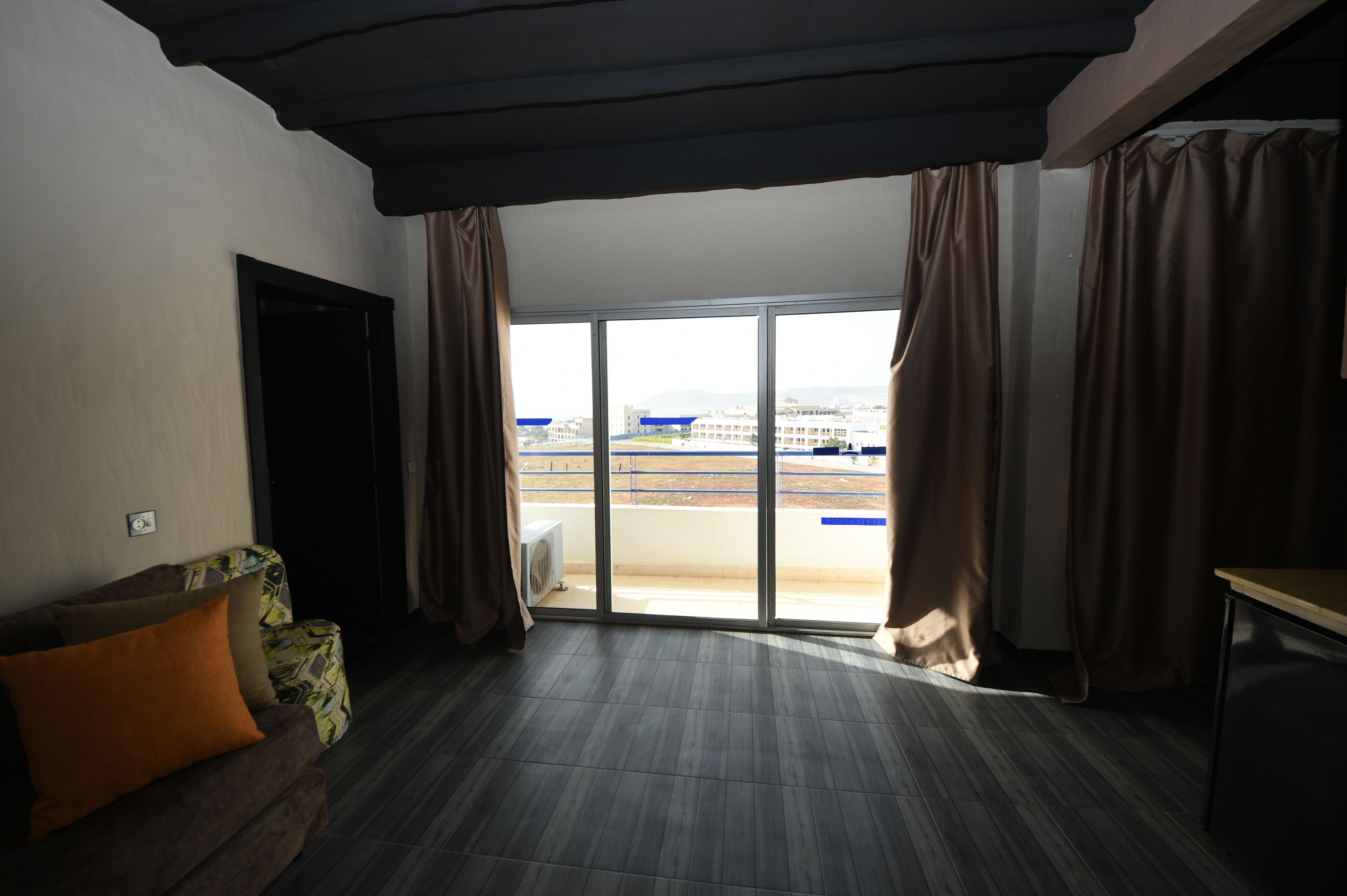 A room with a large sliding glass door leading to a balcony, a sofa with cushions, and a small table.