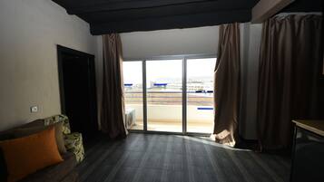 A room with a large sliding glass door leading to a balcony, a sofa with cushions, and a small table.