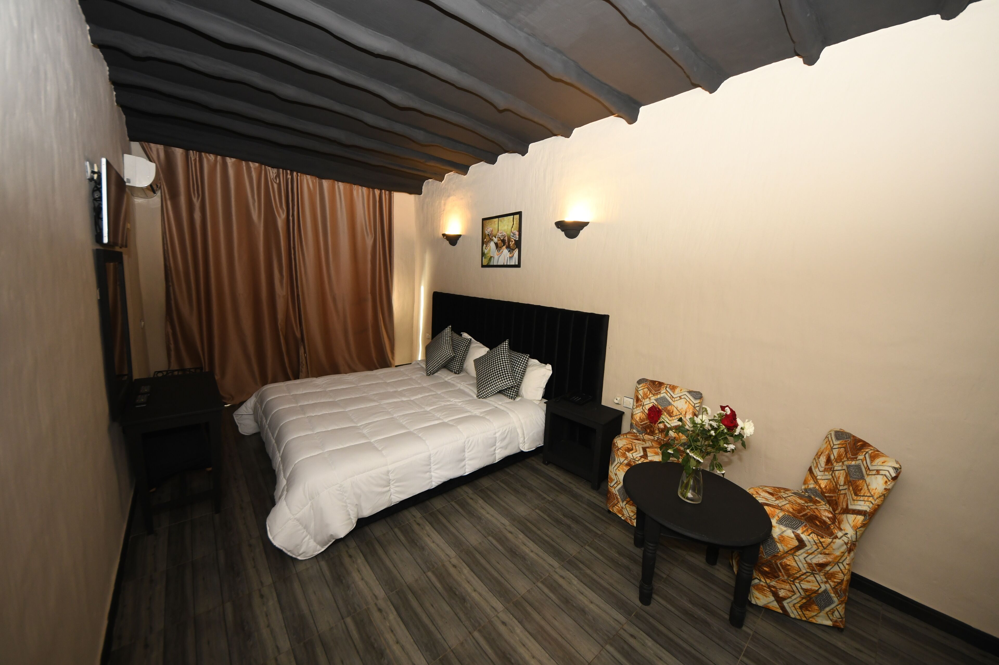A hotel room with a bed, a nightstand, a table with a vase, and a chair.